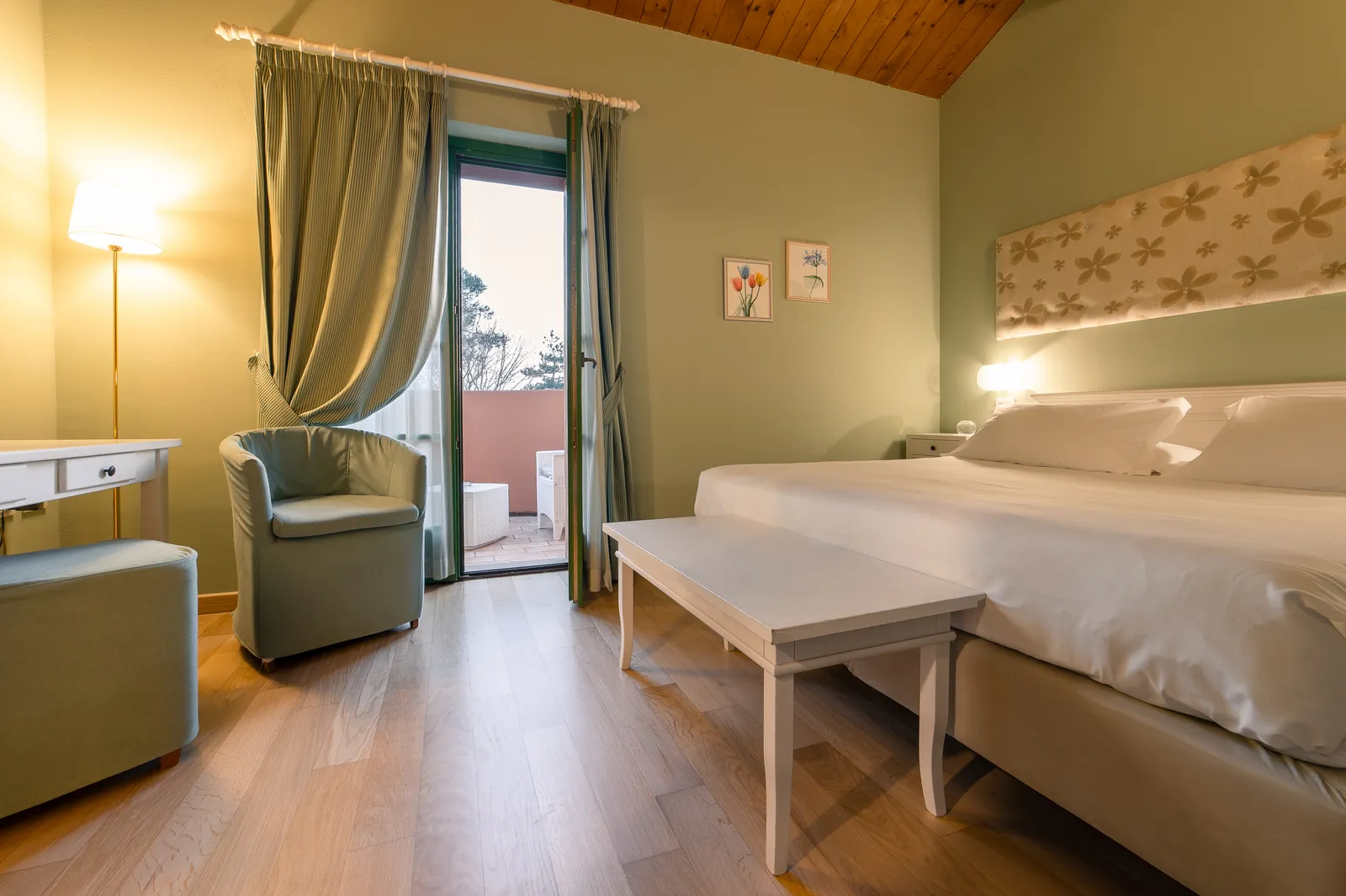 Camera Comfort Deluxe il Fienile con poltrona, tende verdi e porta-finestra sulla terrazza privata affacciata sulla campagna