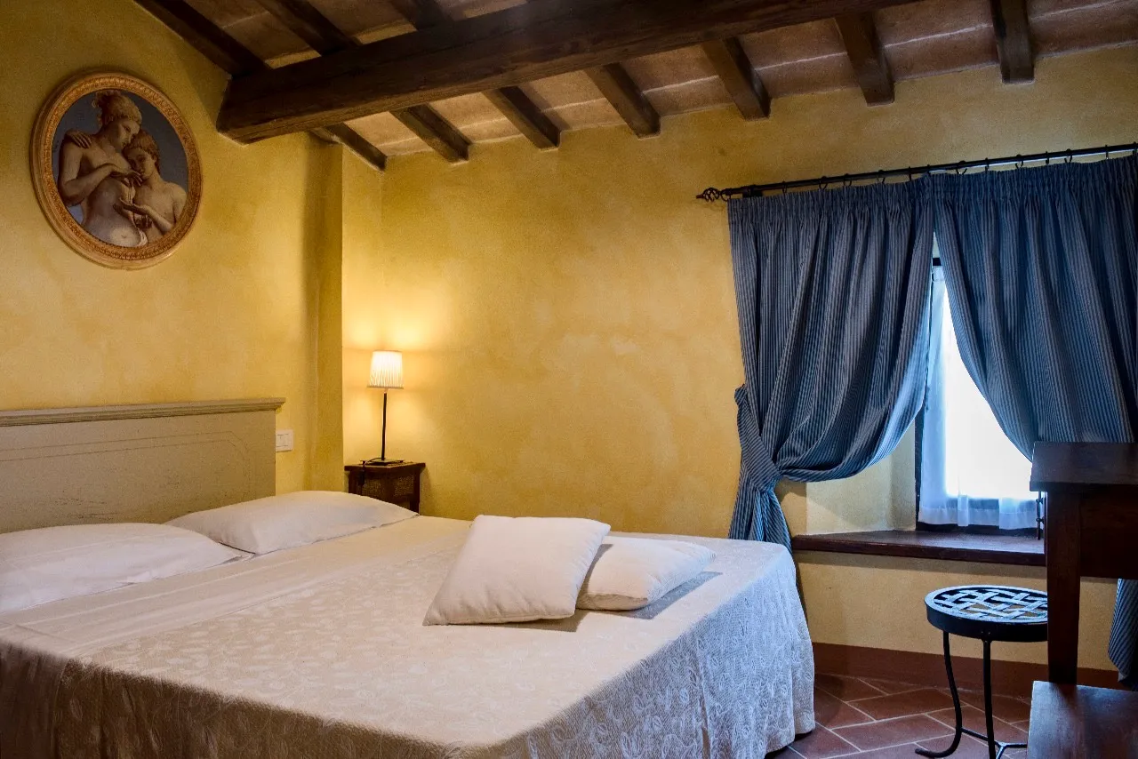 Camera Rurale matrimoniale con parete in mattoni a vista, pavimento in cotto, soffitto travato in legno e letto matrimoniale