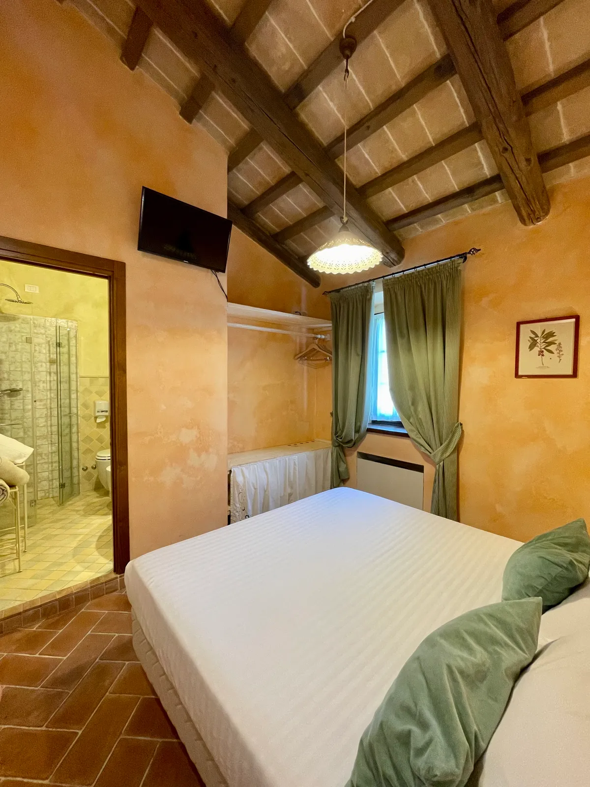 Camera Standard matrimoniale con lampadario, testiera verde imbottita, soffitto a travi e finestra sulla campagna