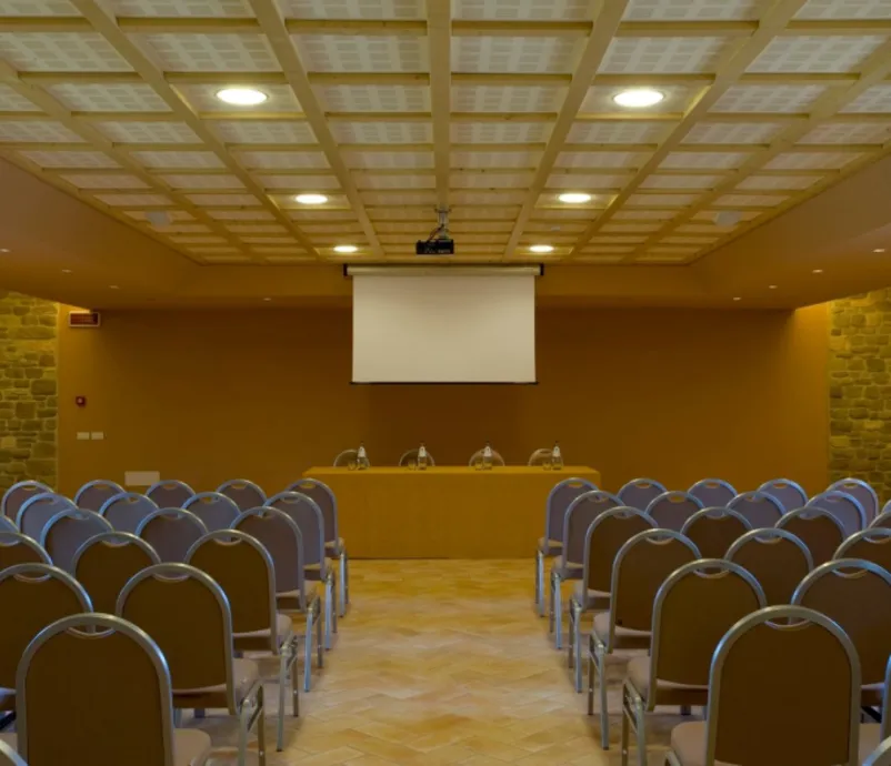 Sala Il Convivio allestita a platea per meeting e congressi, con schermo per proiezioni e pareti in pietra